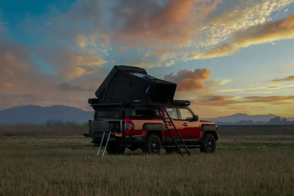 Red off-road ute with rooftop tent parked in an open field at sunset for outdoor adventure travel